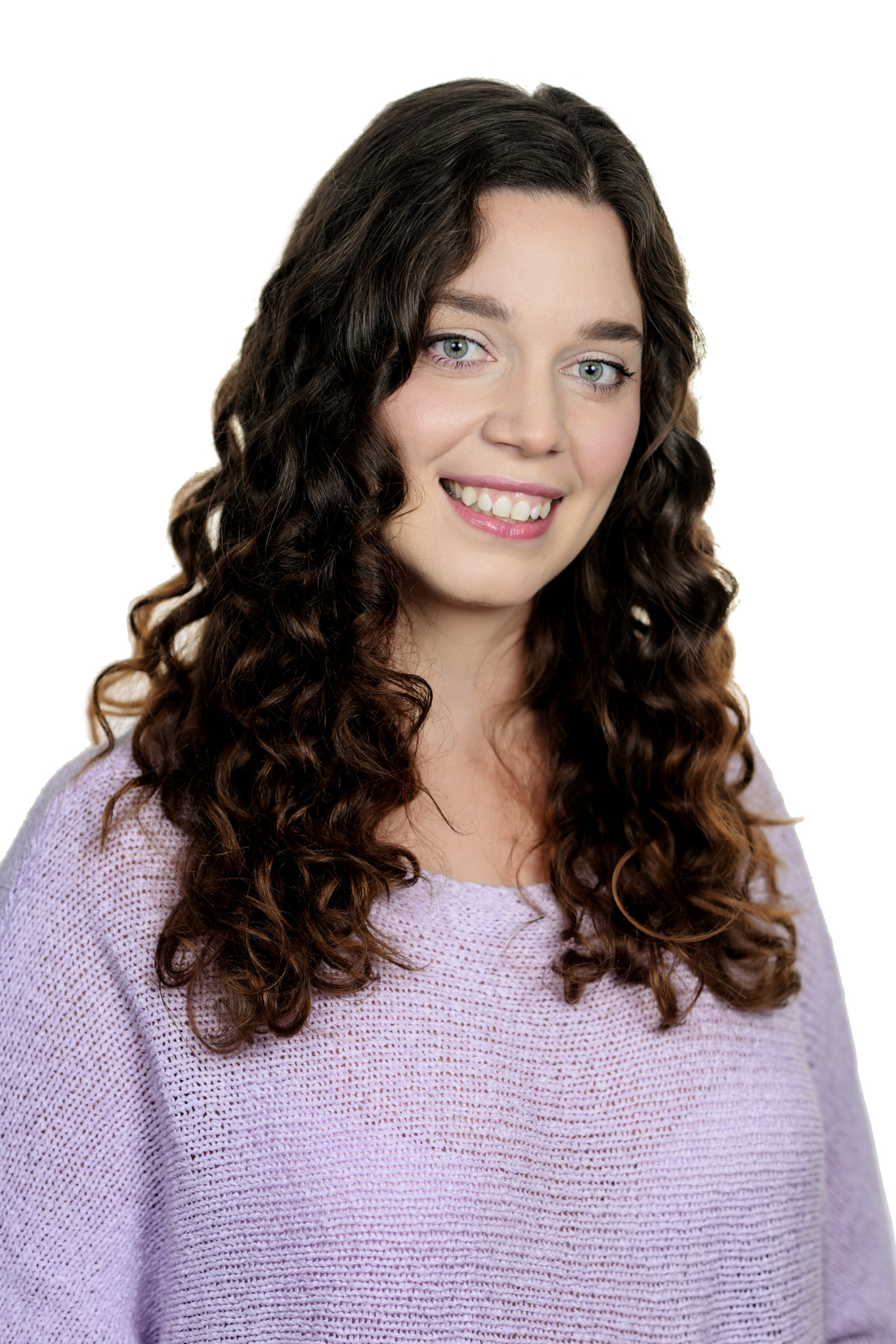 Smiling young woman with long, dark curly hair wearing a lavender knit sweater against a white background.